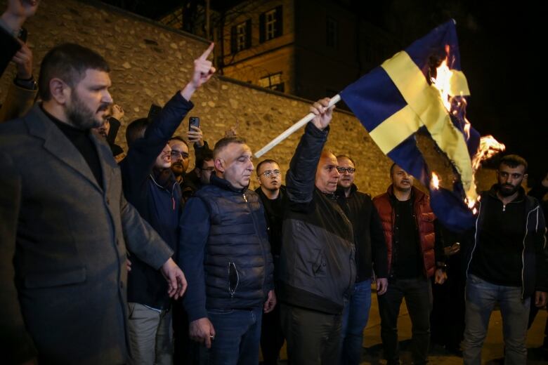 A man within a larger group holds a burning flag.