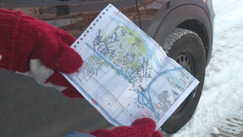 a person wearing red canada mittens holds a paper map with blue pen on it 