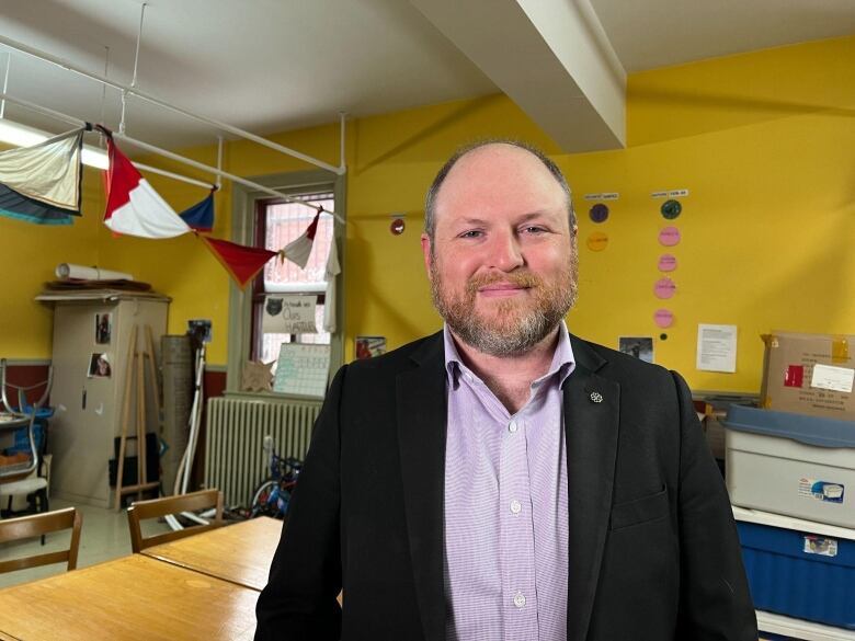 Craig Sauv wearing a black blazer standing in a yellow room.