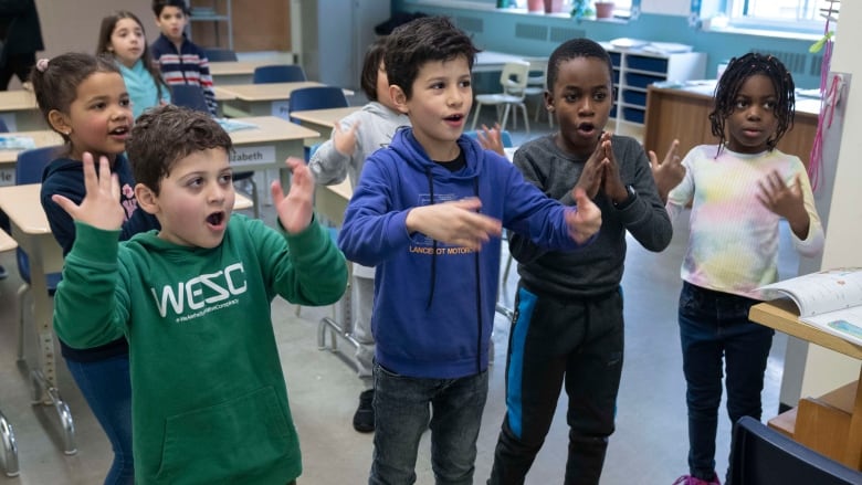 Students standing up and singing in a classroom. 