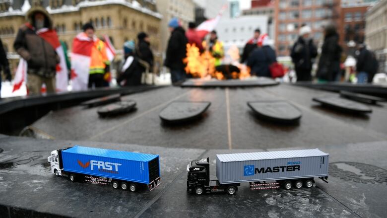 Two small toy trucks on the rim of a ceremonial firepit.