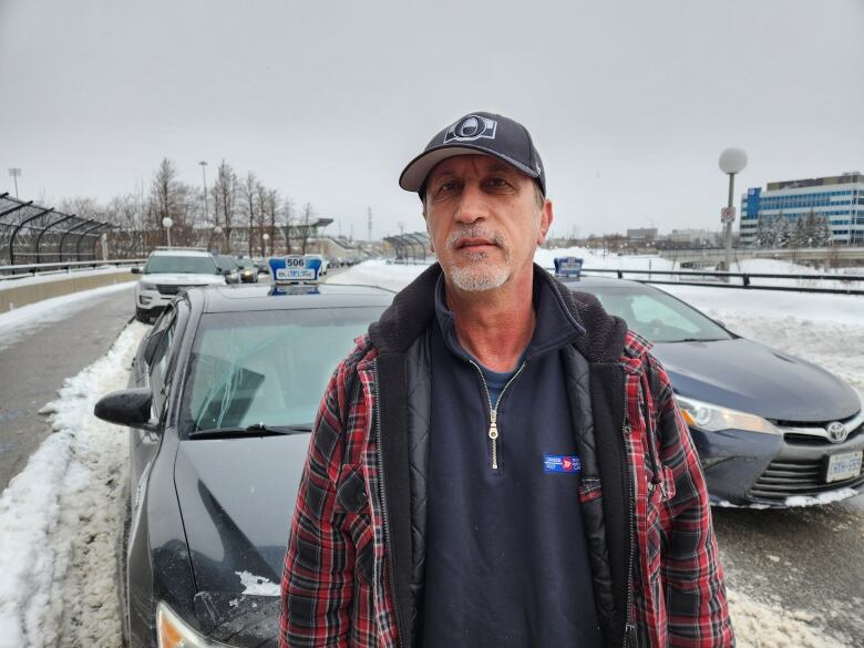 Man in plaid jacket stands in front of taxi. 