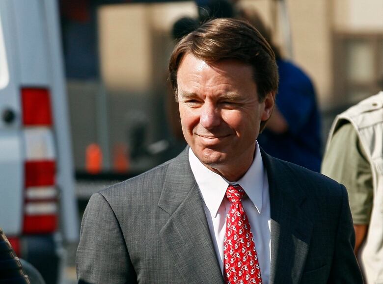 A man in a suit and red tie is shown in an outdoor setting.