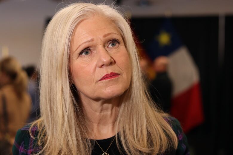 A woman looks up to the right with an Acadian flag in the background.