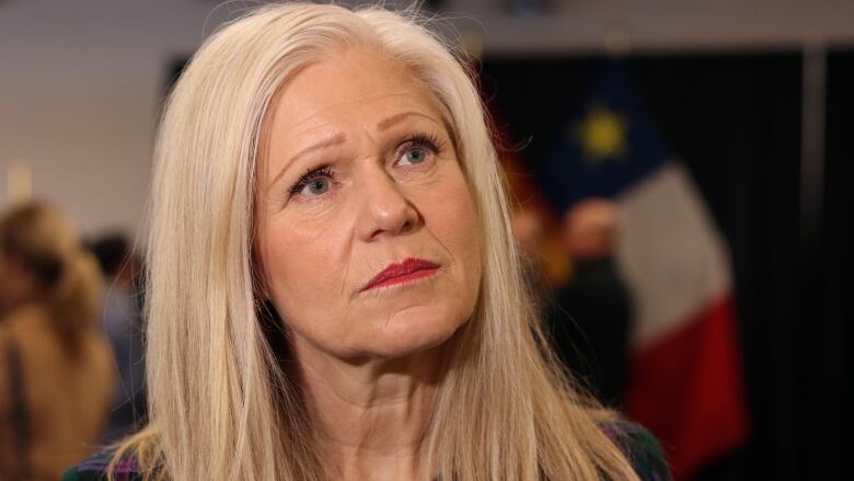 A woman looks up to the right with an Acadian flag in the background.