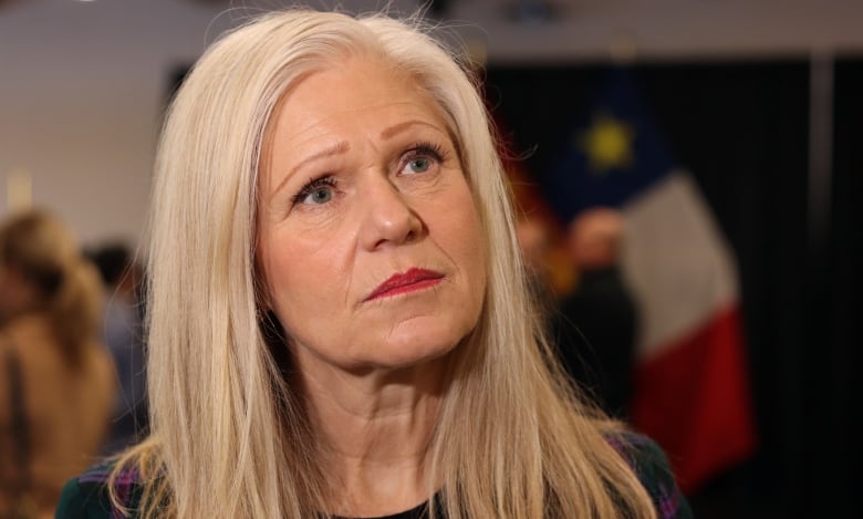 A woman looks up to the right with an Acadian flag in the background.