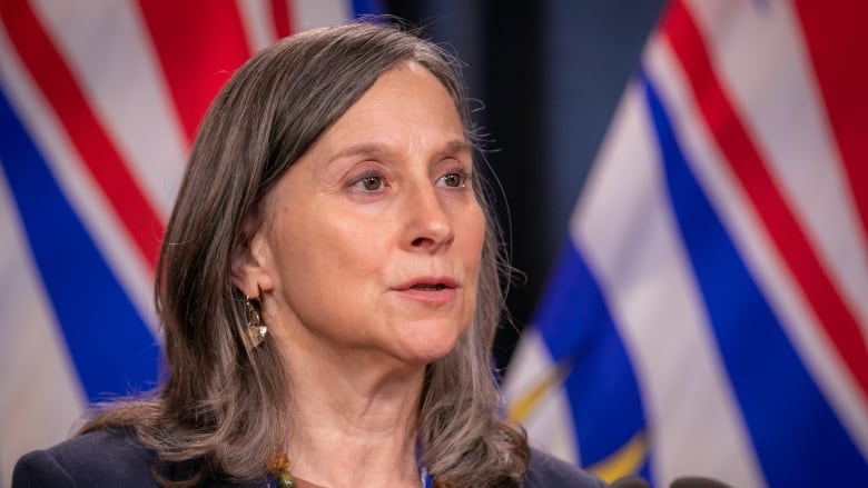 A woman with shoulder-length grey hair stands at a podium.