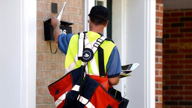 Postal worker seen from the back as he puts mail into a mailbox at a suburban house entrance.