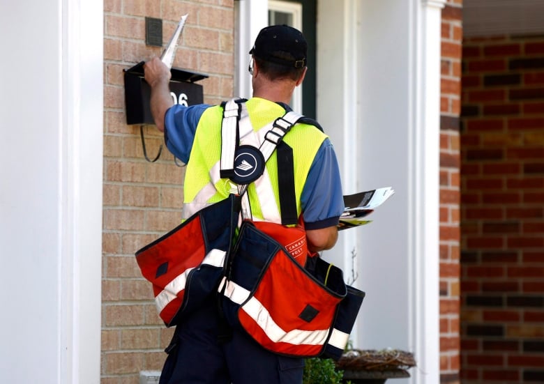 Postal worker seen from the back as he puts mail into a mailbox at a suburban house entrance.