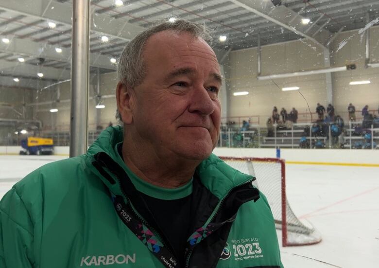 A man stands smiling in a hockey arena. 