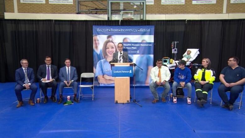 Many people are seen sitting at a stage with a podium in the middle.