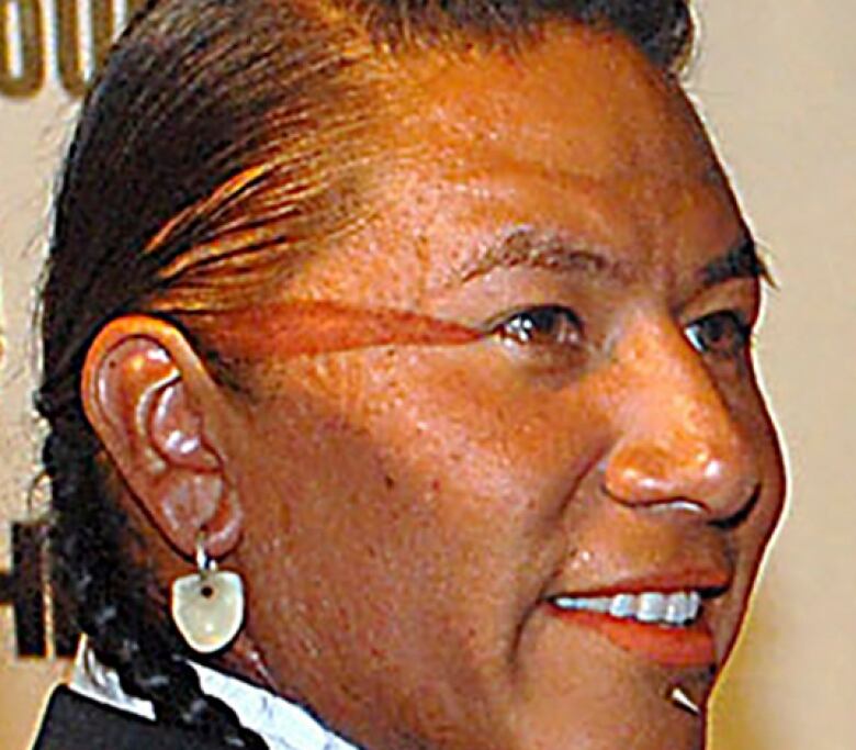 An Indigenous man with braided hair and an earring wearing a dark jacket.