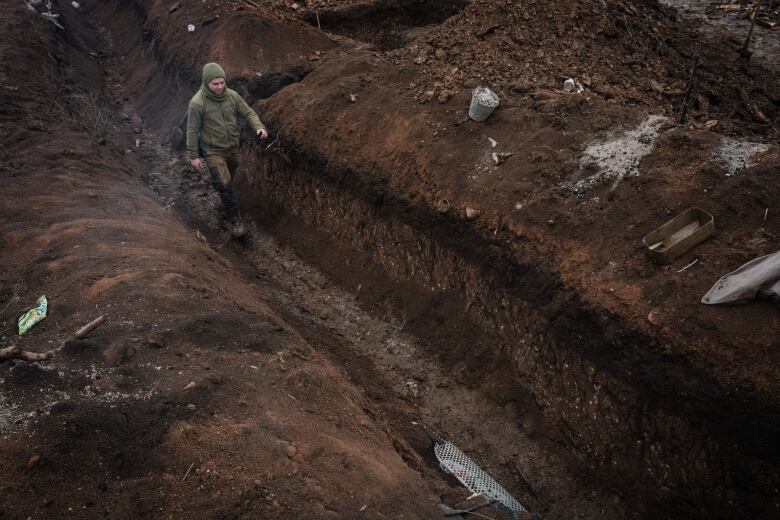 A man walks in a waist-deep trench that cuts diagonally across the image. 