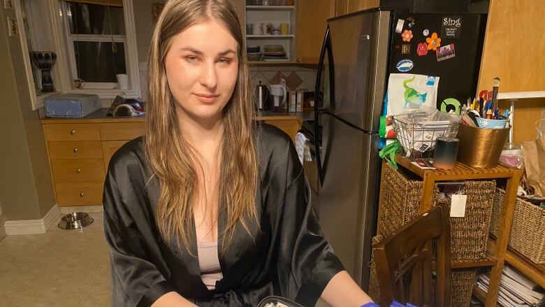 A woman stands in her kitchen in a black robe holding a prescription opioid kit, including sanitizing wipes, bottles and needles.