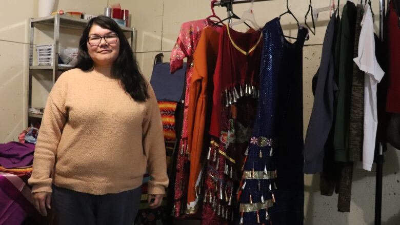 A woman stands next to her collection of jingle dresses, which show off a variety of colours.