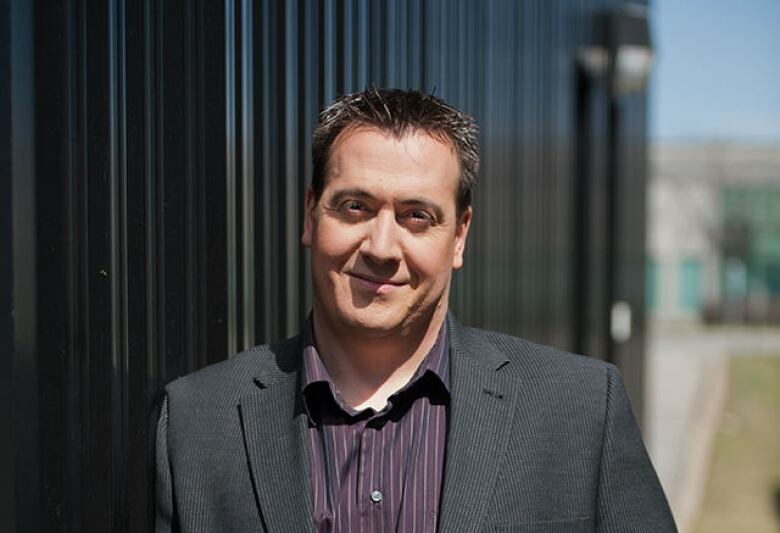 Portrait of a man smiling, leaning on a wall, outdoors.