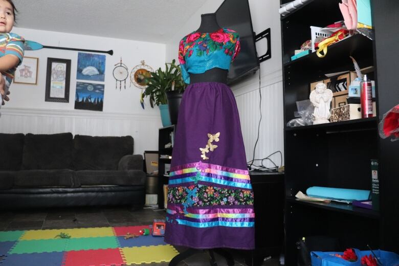 A mannequin wears a purple dress with golden butterlies and ribbons ranging from violet to blue.