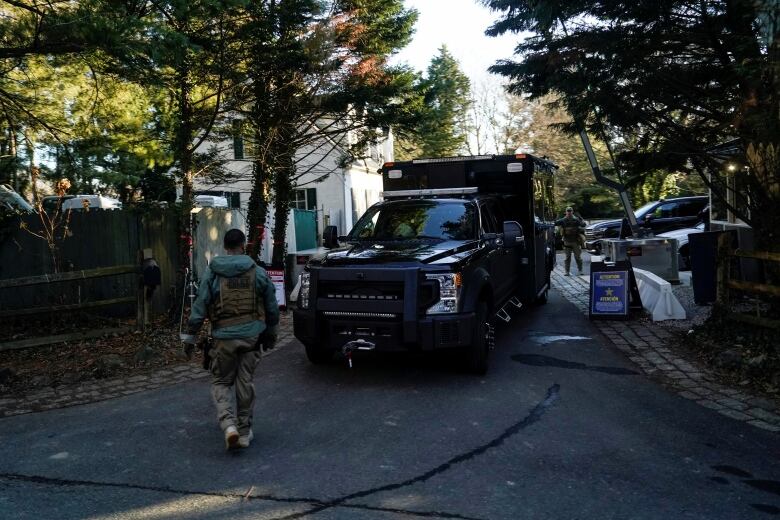 Two people wearing camouflage clothing are seen near a dark-coloured truck in a driveway.