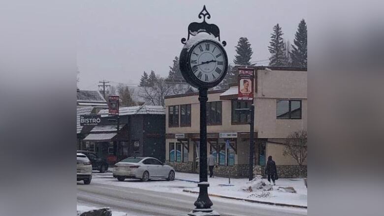 A freestanding black-and-white clock on the street with snow.