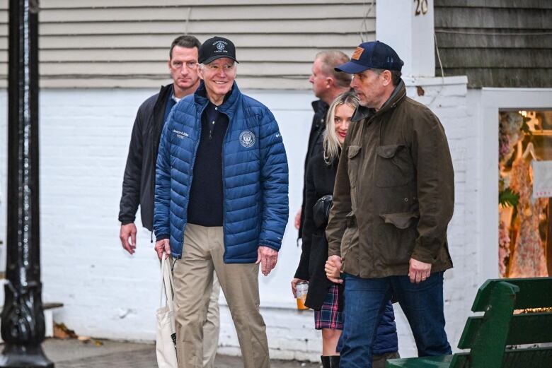 Two men in baseball caps and coats are shown walking outside. Other people are shown behind them.