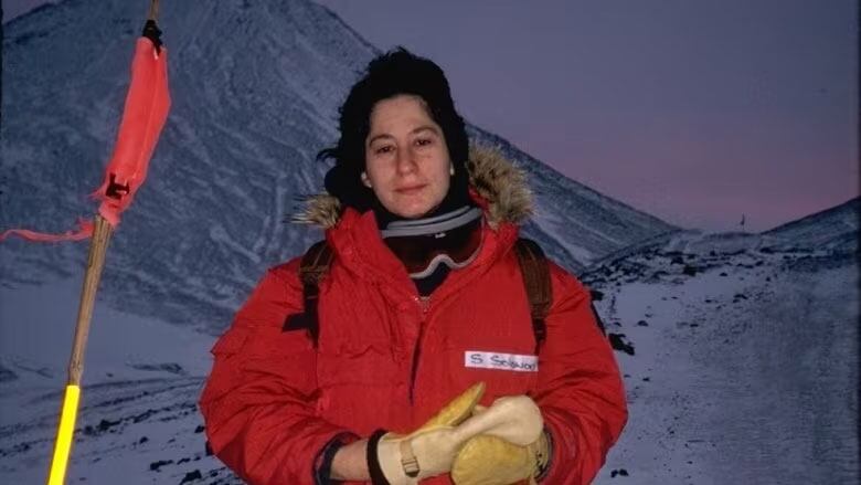 A female scientist is standing in a red parka in the Arctic.