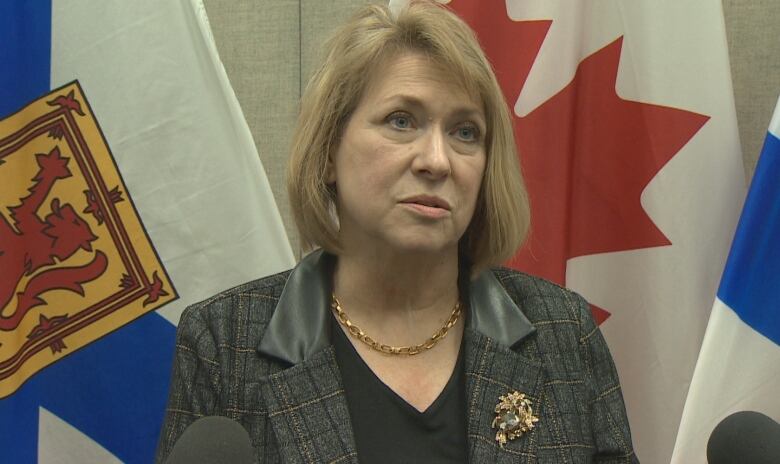 A woman with blond hair stands in front of the Canadian and Nova Scotia flags.