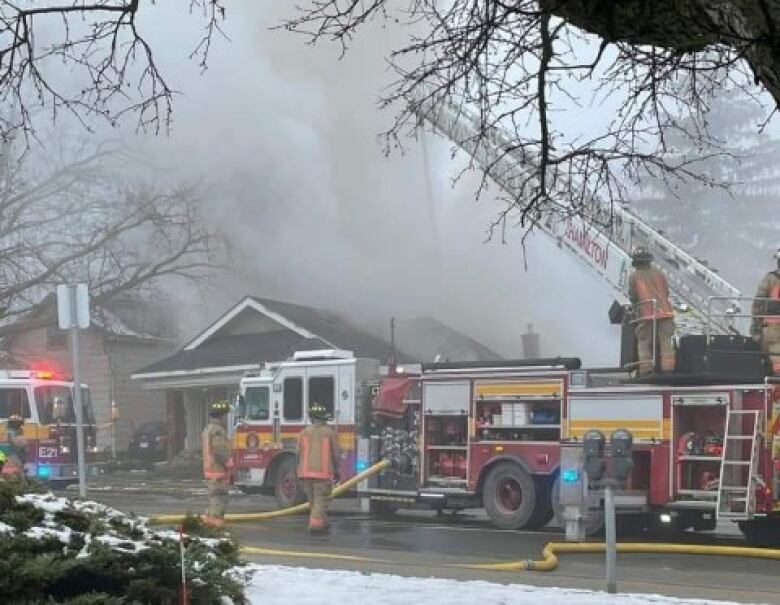 A fire truck and firefighters outside a house on fire with smoke overhead.