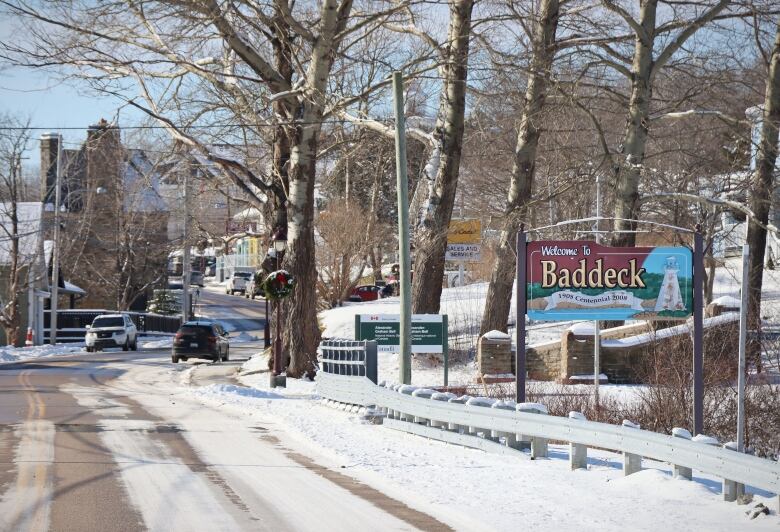 A snowy roadway with two cars driving in opposite directions. There is a sign on the right side of the street that says, 