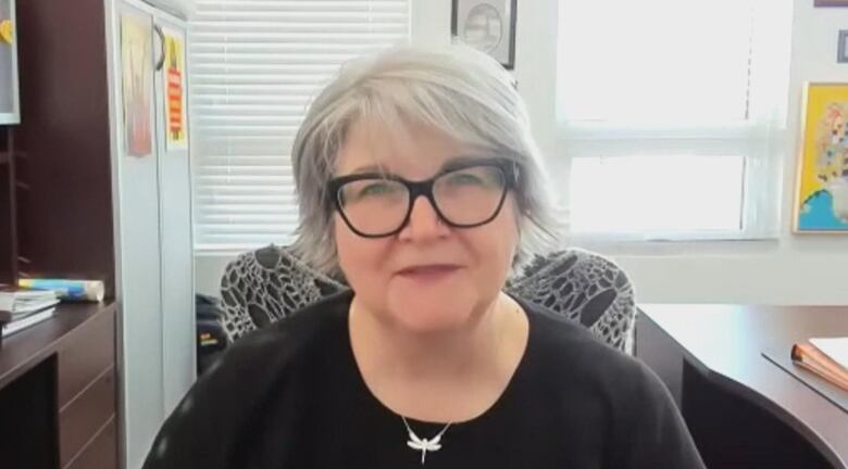 A woman with short hair and glasses stares out while sitting in an office. 