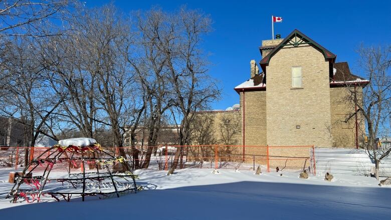 A large brick building can be seen across an empty filed filled with snow. 