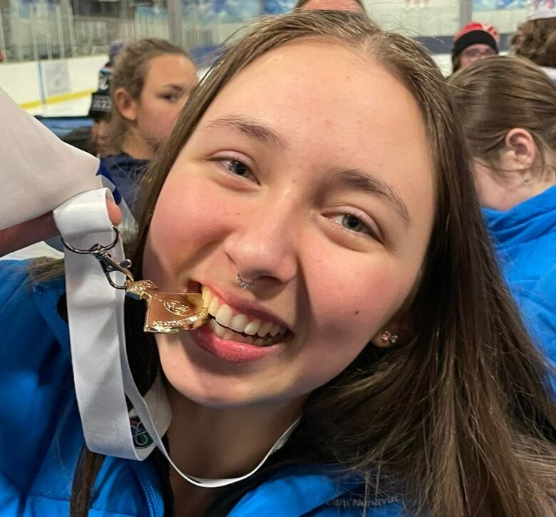 Girl biting gold ulu medal.