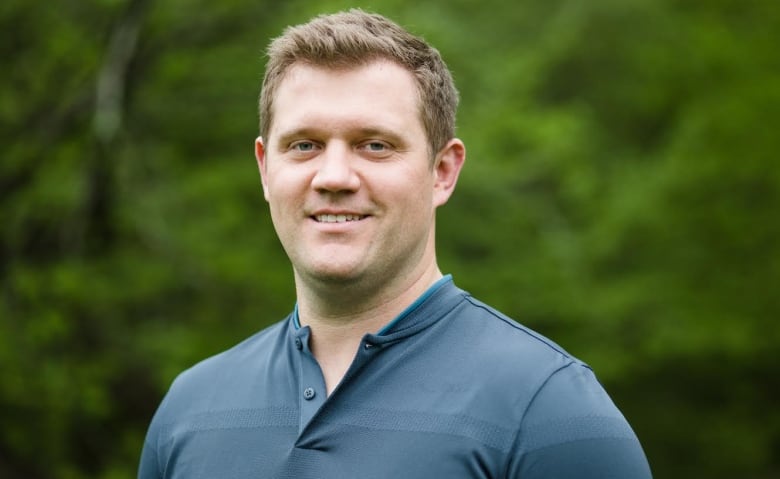 A man in a blue shirt in front of a blurry green background