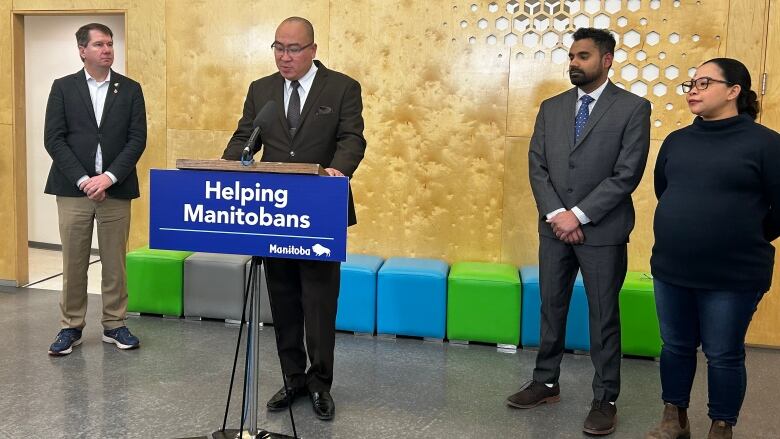 A man speaks at a podium while three other people stand nearby.