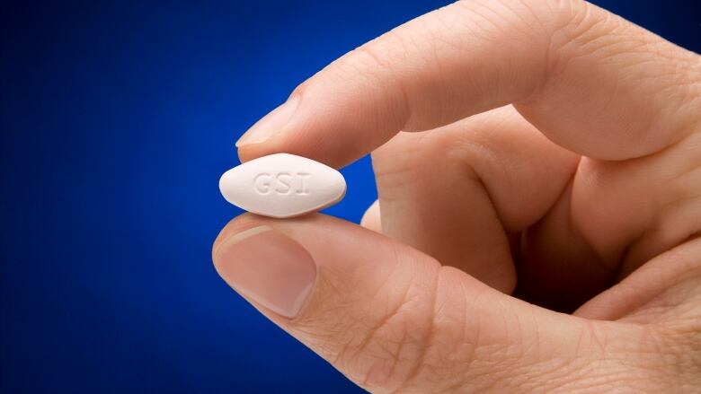 A closeup shows a person holding a small pill with the letters 