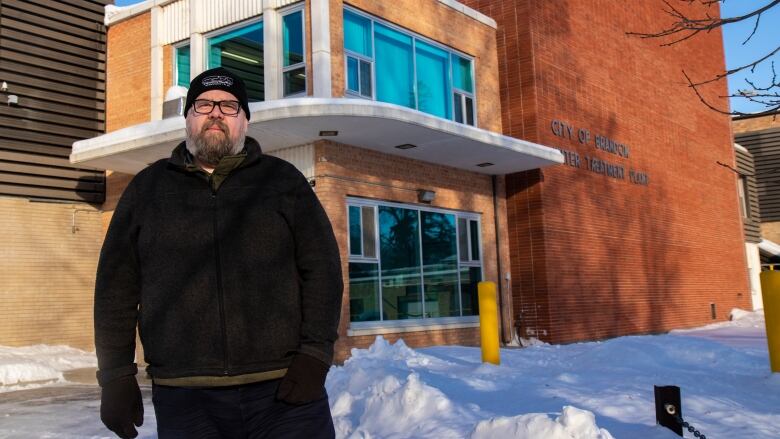 A man in a toque with a beard stands in front of a water treatment plant.