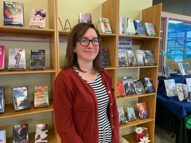 A woman with glasses stands in front of a library bookshelf.