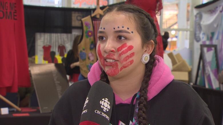 A woman stands with a red handprint painted on her face. 