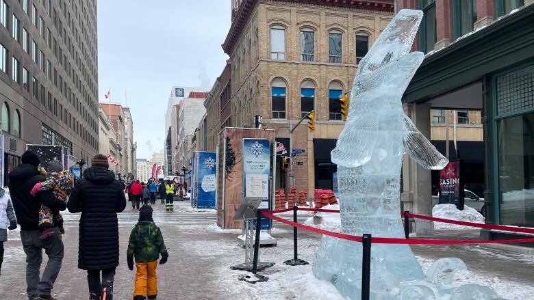 People walk on a city pedestrian street in winter next to a ice sculpture of a large fish.