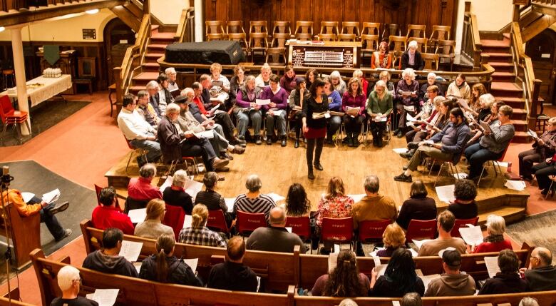 A group of people sit in the middle of a church in a half-circle, performing in front of an audience.