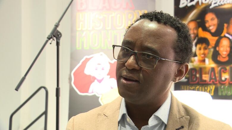 A Black man wearing glasses and a suit poses for the camera.