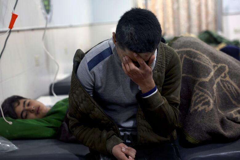 Earthquake victims, including a man sitting on a cot next to a young patient, are treated at the al-Rahma Hospital in Karkush town, in northern Syria.