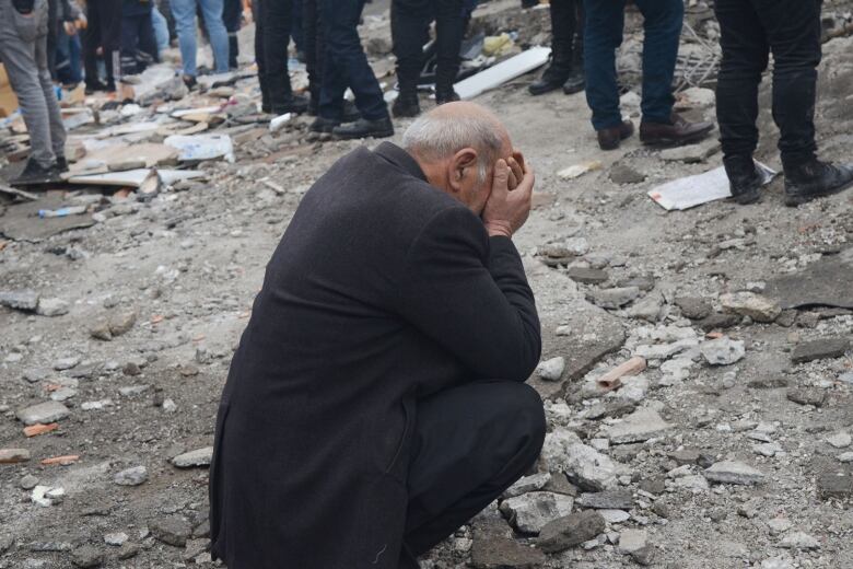 A man crouching on rubble buries his hands in his face, as people search for survivors in the rubble following an earthquake in Diyarbakir, in southeastern Turkey.