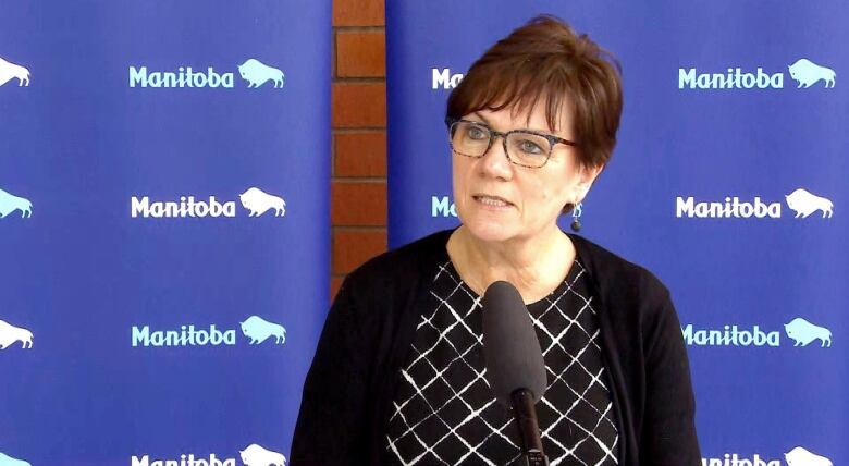 A lady stands and speaks into a microphone in front of a blue background.