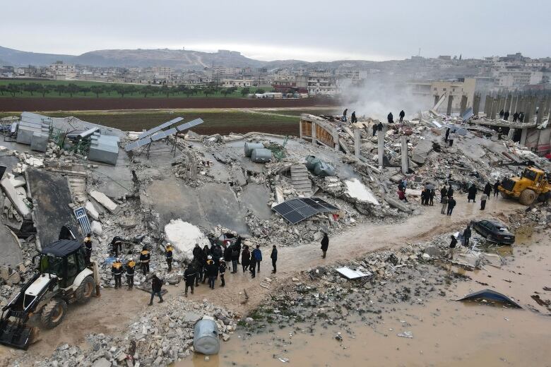 An aerial view of workers standing on a large pile of concrete rubble.