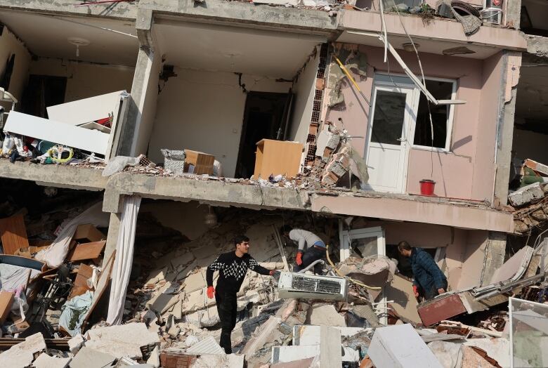 A man in a black and white sweater sifts through the rubble of a house following an earthquake in Turkey.