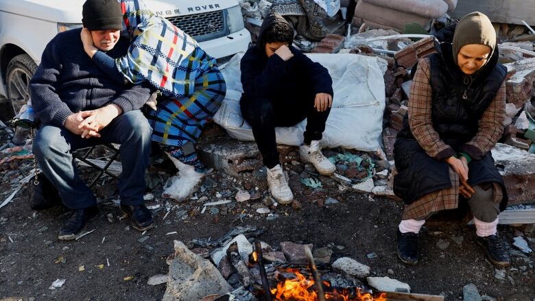 People huddle around a makeshift fire to stay warm and behind them is a litter of furniture and Range Rover, in the aftermath of a deadly earthquake in Turkey.