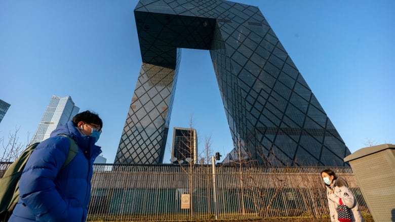 In this Thursday, Feb. 4, 2021 file photo, people wearing face masks to protect against the spread of the coronavirus, walk past the CCTV Headquarters building, the home of Chinese state-run television network CCTV and its overseas arm CGTN, in Beijing. The U.K. has stripped China's state-owned TV channel of its broadcasting license in the country, after an investigation found the license holder lacked editorial control and had links to China's ruling Communist Party.