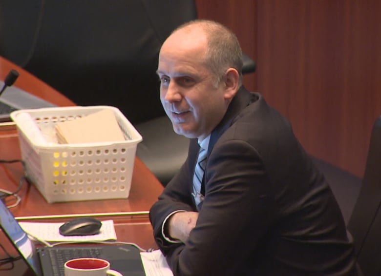 Man sits with his arms folded, smiling, at a desk in City Hall.