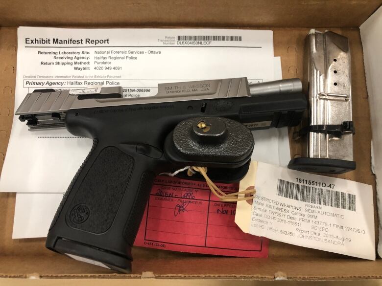 A gun with tags on it lies in a cardboard box.