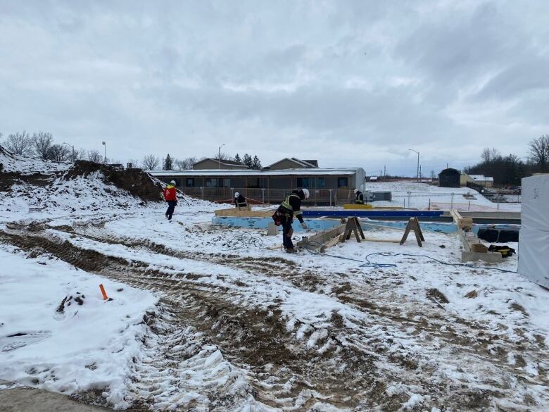 Workers walk on a snowy, outdoor site. 